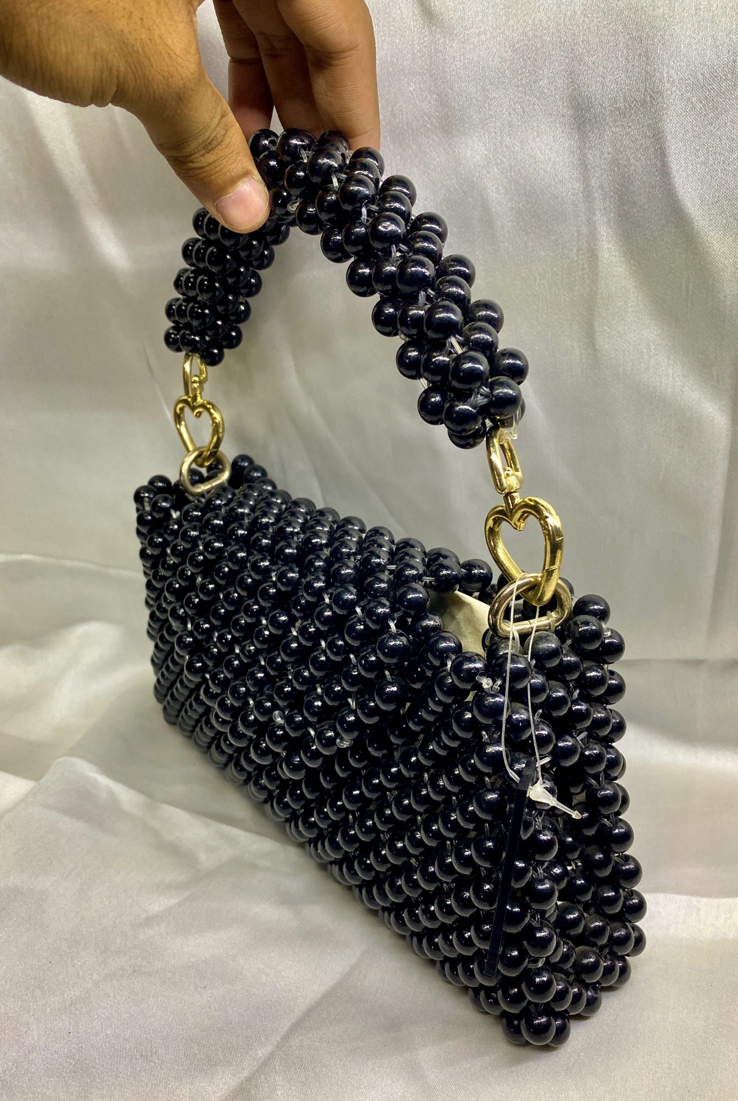 Black beaded handbag with gold accents held by a hand on a light background