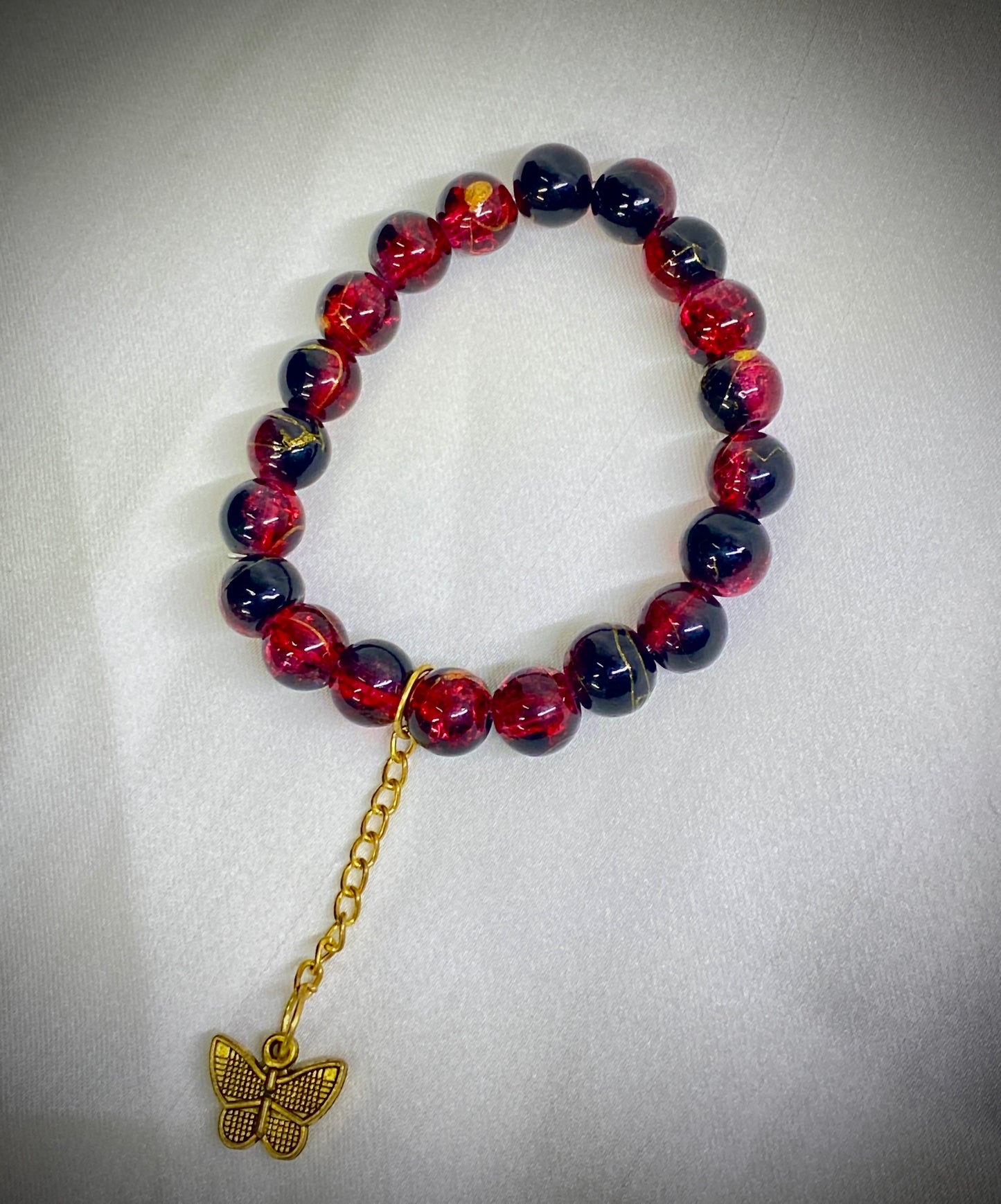 Beaded bracelet with red and blue beads and a gold butterfly charm on a light gray background