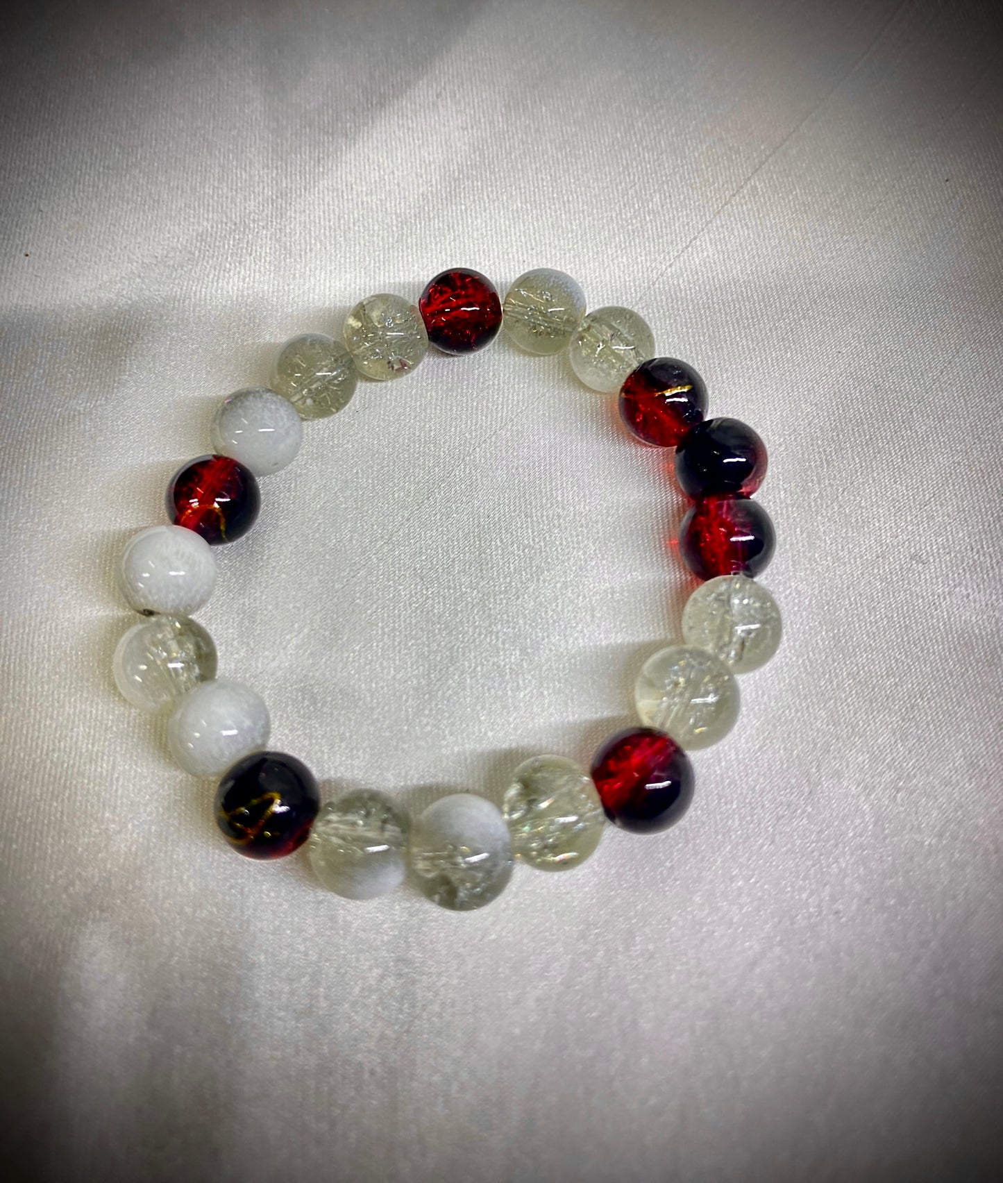 Beaded bracelet with red, black, and clear beads on a white fabric background