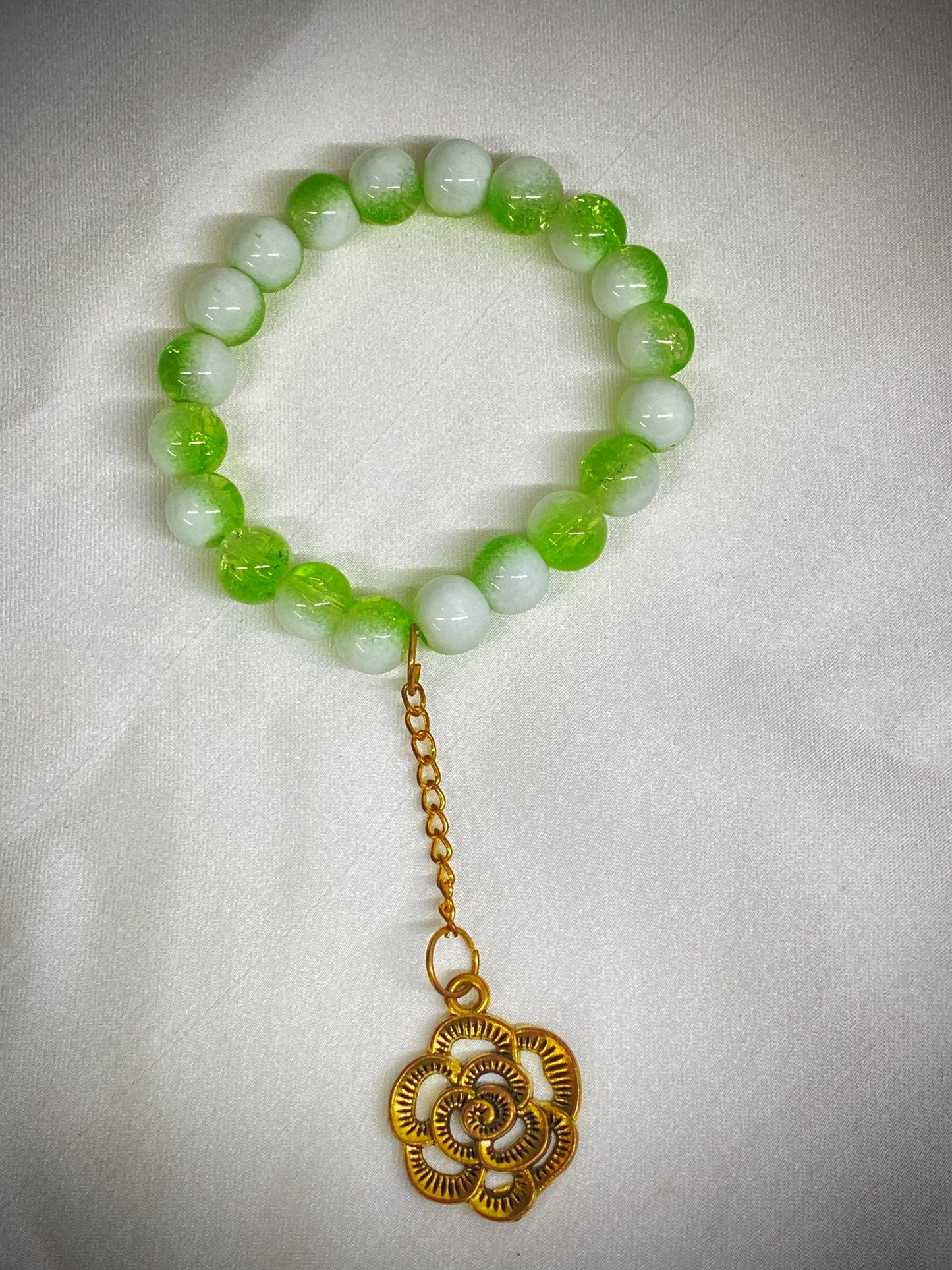 Green beaded bracelet with a gold charm on a white background