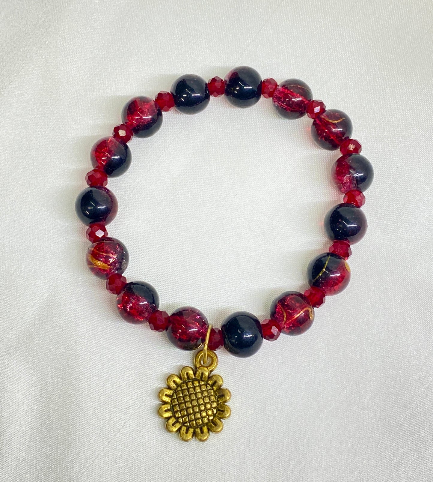 Bracelet with red and black beads and a gold sunflower charm on a white background