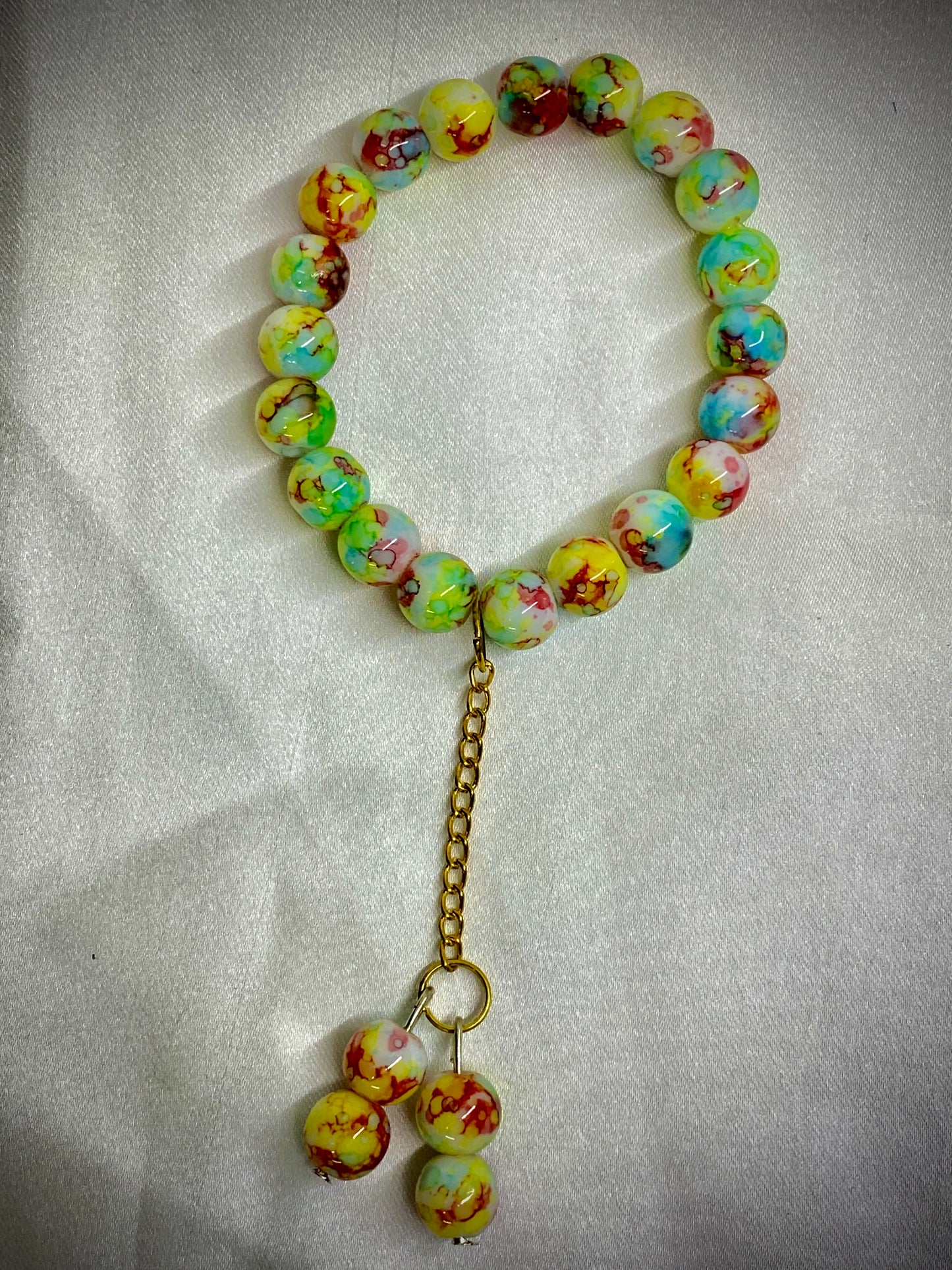 Colorful beaded bracelet with a gold chain on a light fabric background