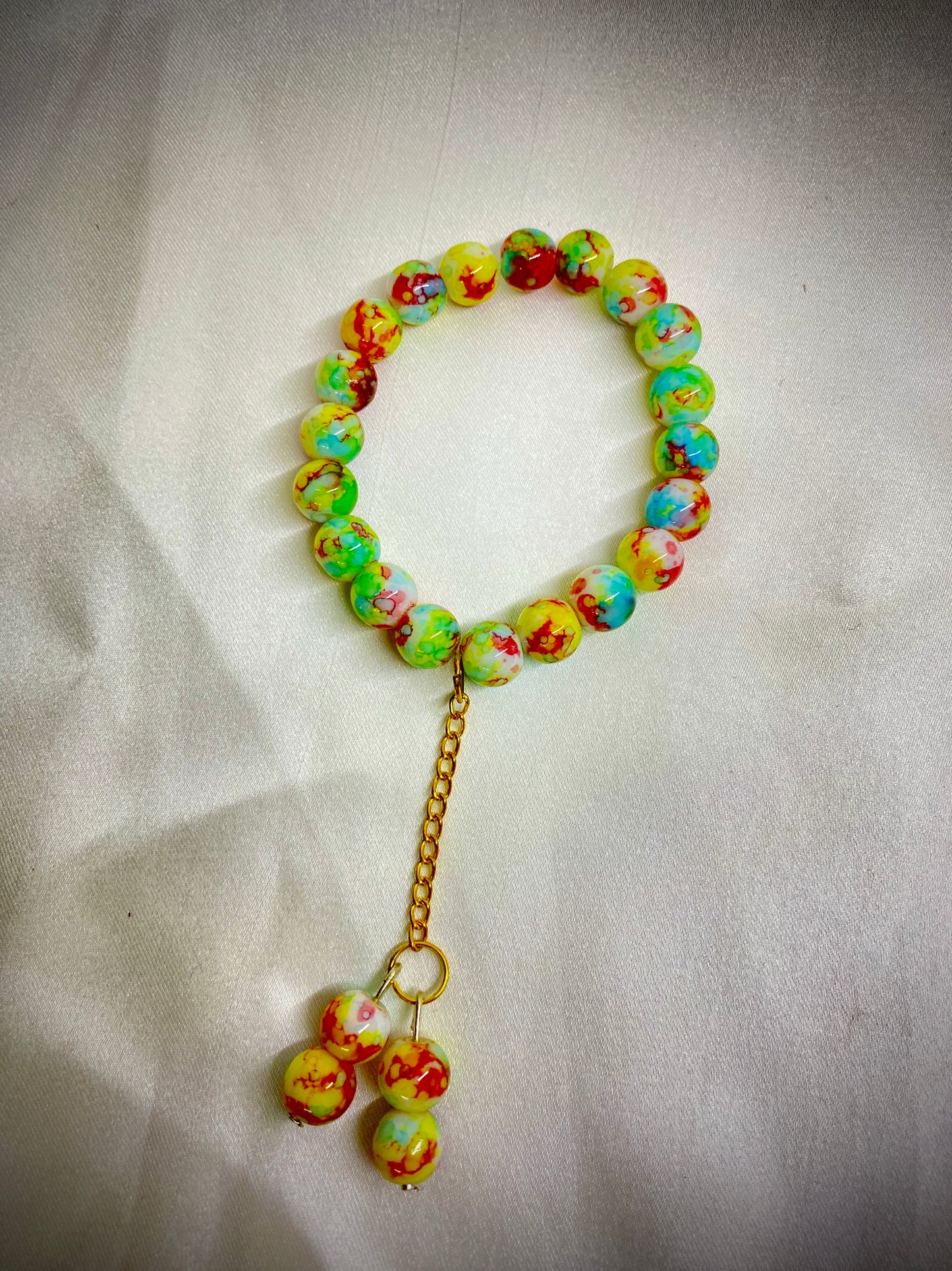 Colorful beaded bracelet with a gold chain and small charms on a light fabric background
