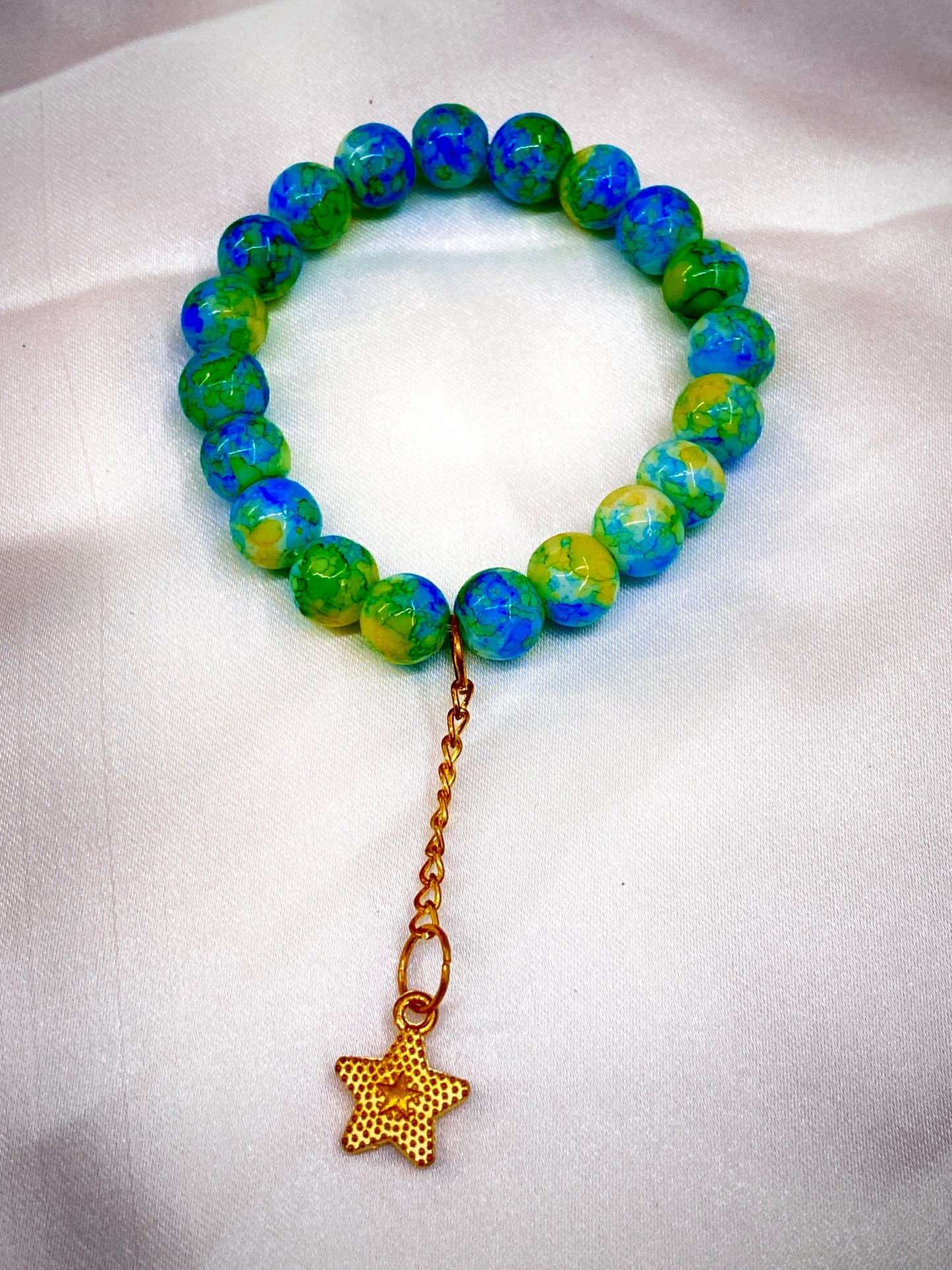 Green and blue beaded bracelet with a gold star charm on a white background