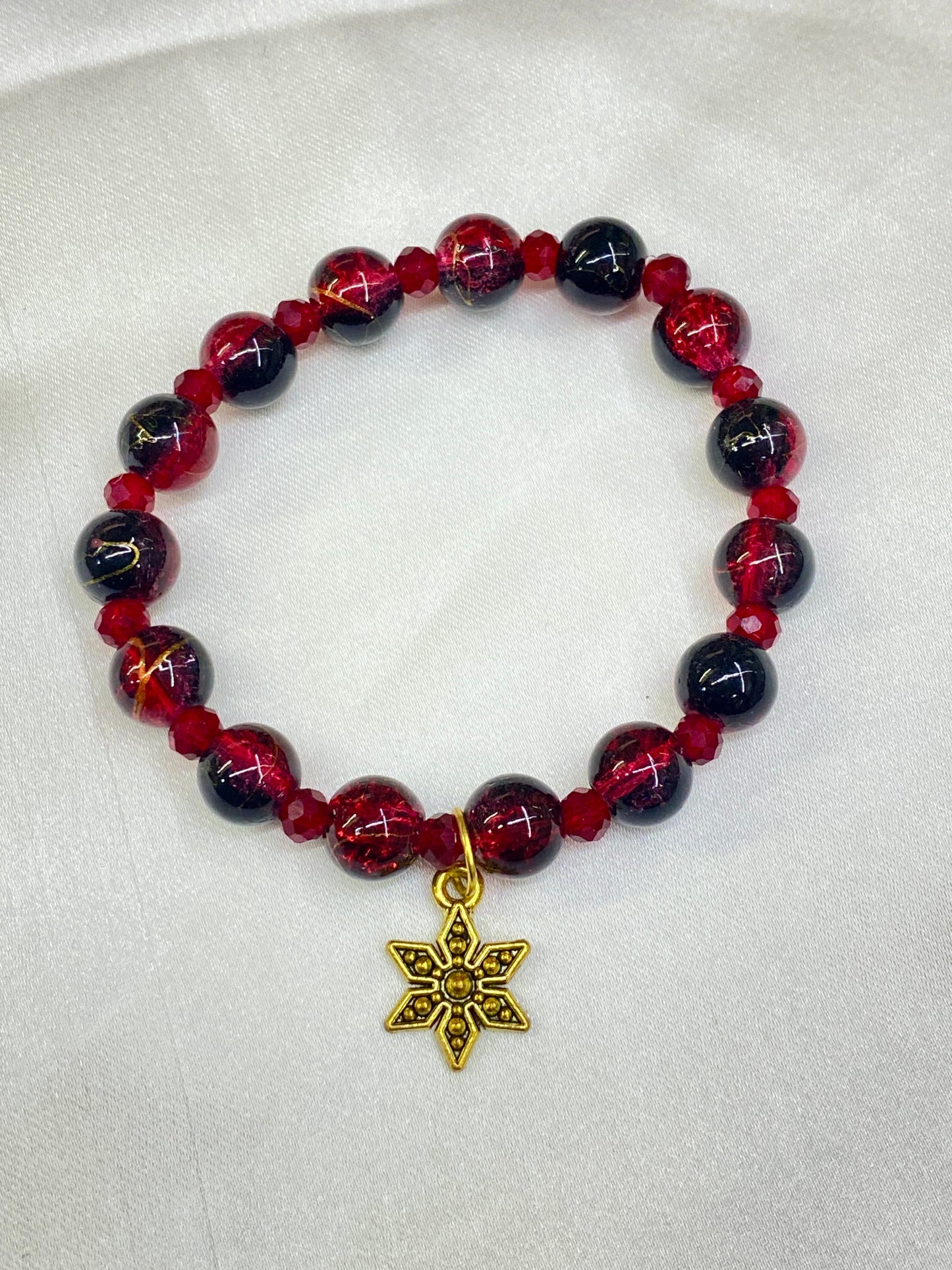 Bracelet with red and black beads and a gold star-shaped charm on a light gray background