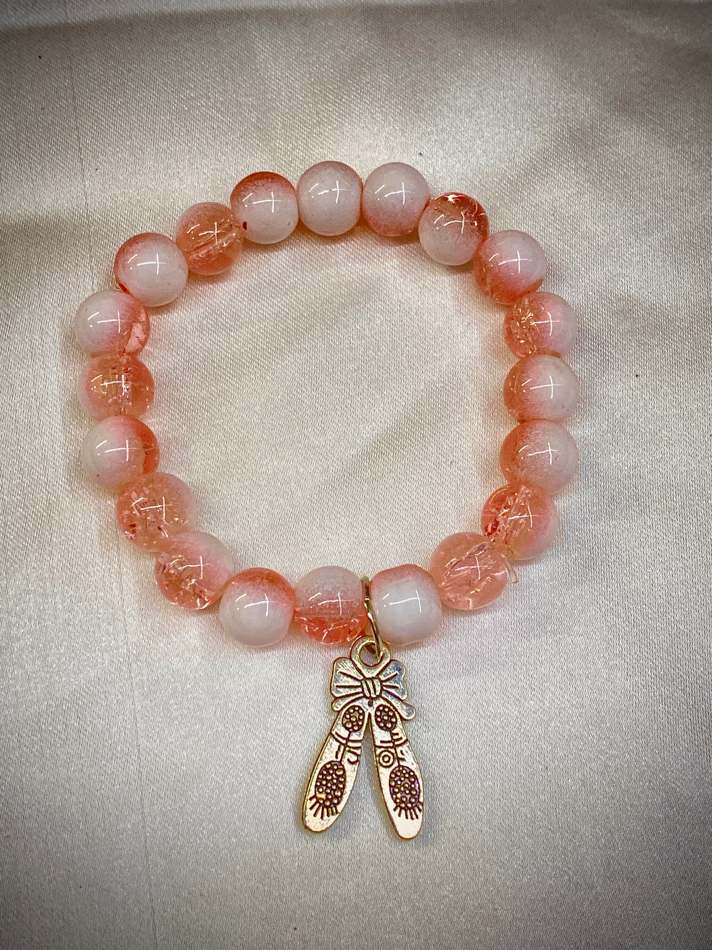 Beaded bracelet with pink and white beads and a gold charm on a light fabric background