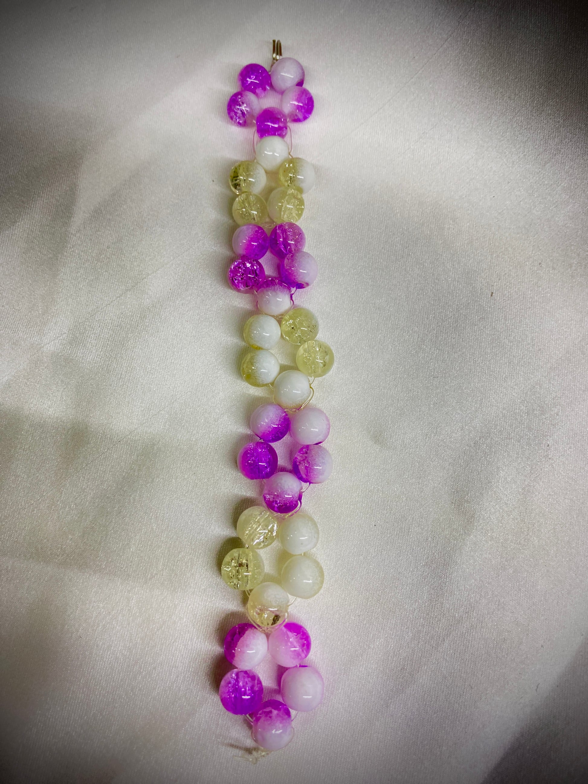 Beaded bracelet with purple, green, and white beads on a light fabric background
