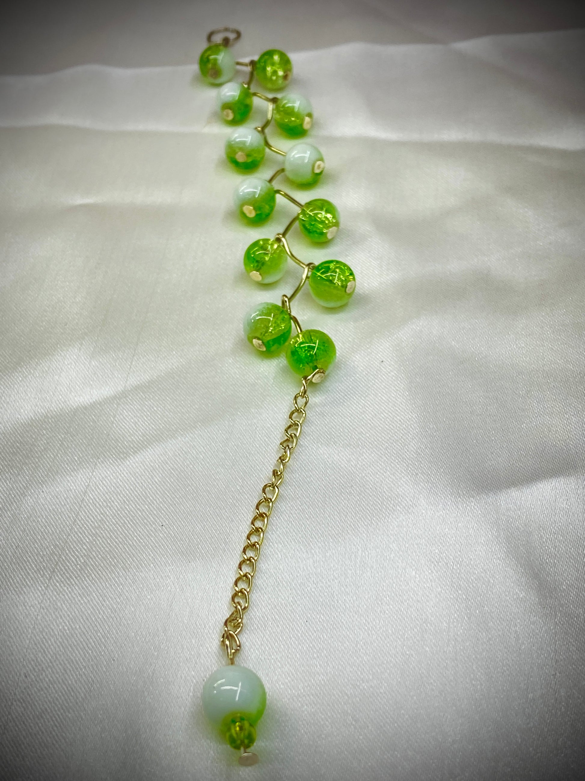 Green beaded earring with gold chain on a white fabric background