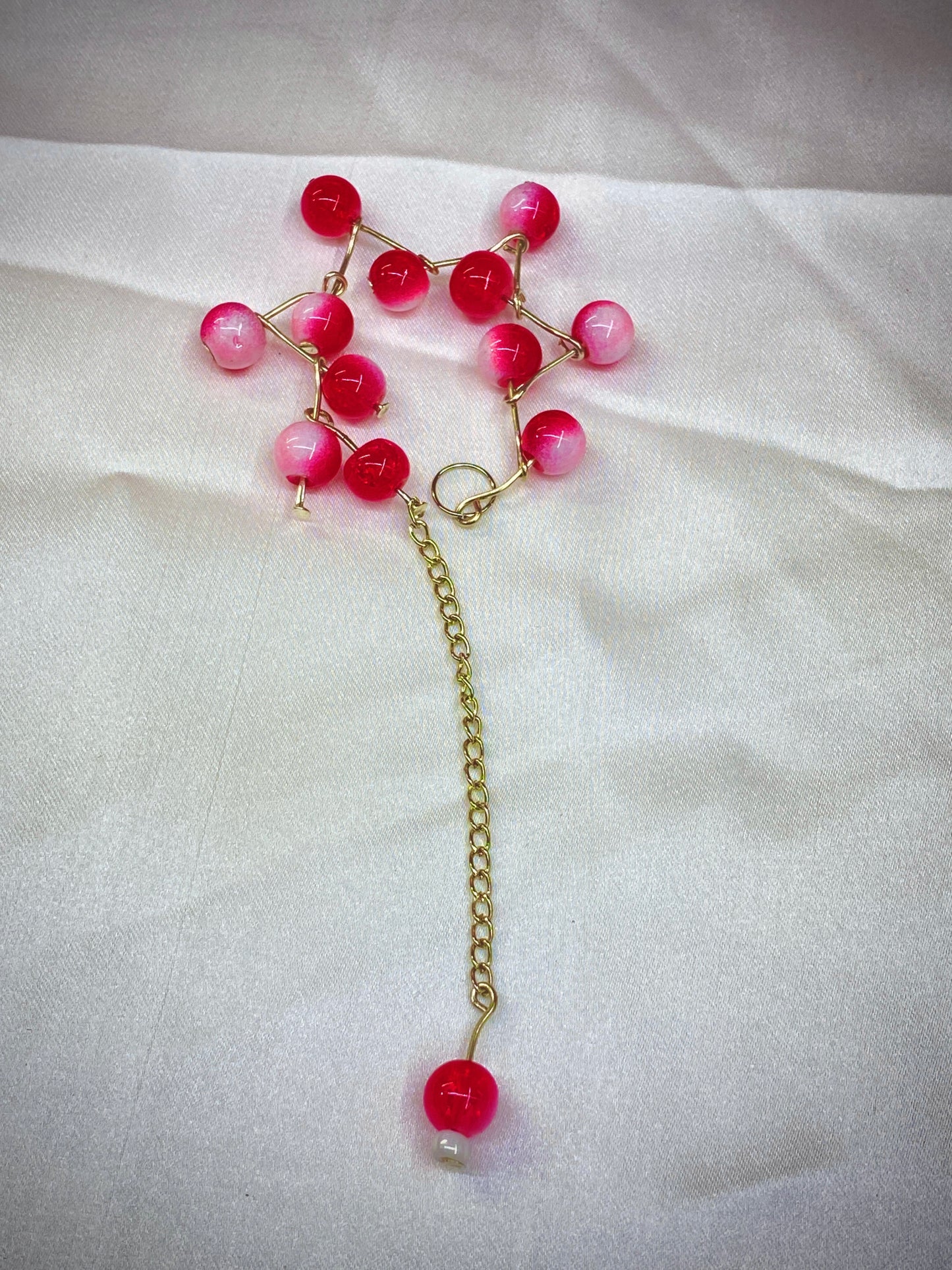 Necklace with pink beads and a gold chain on a white fabric background