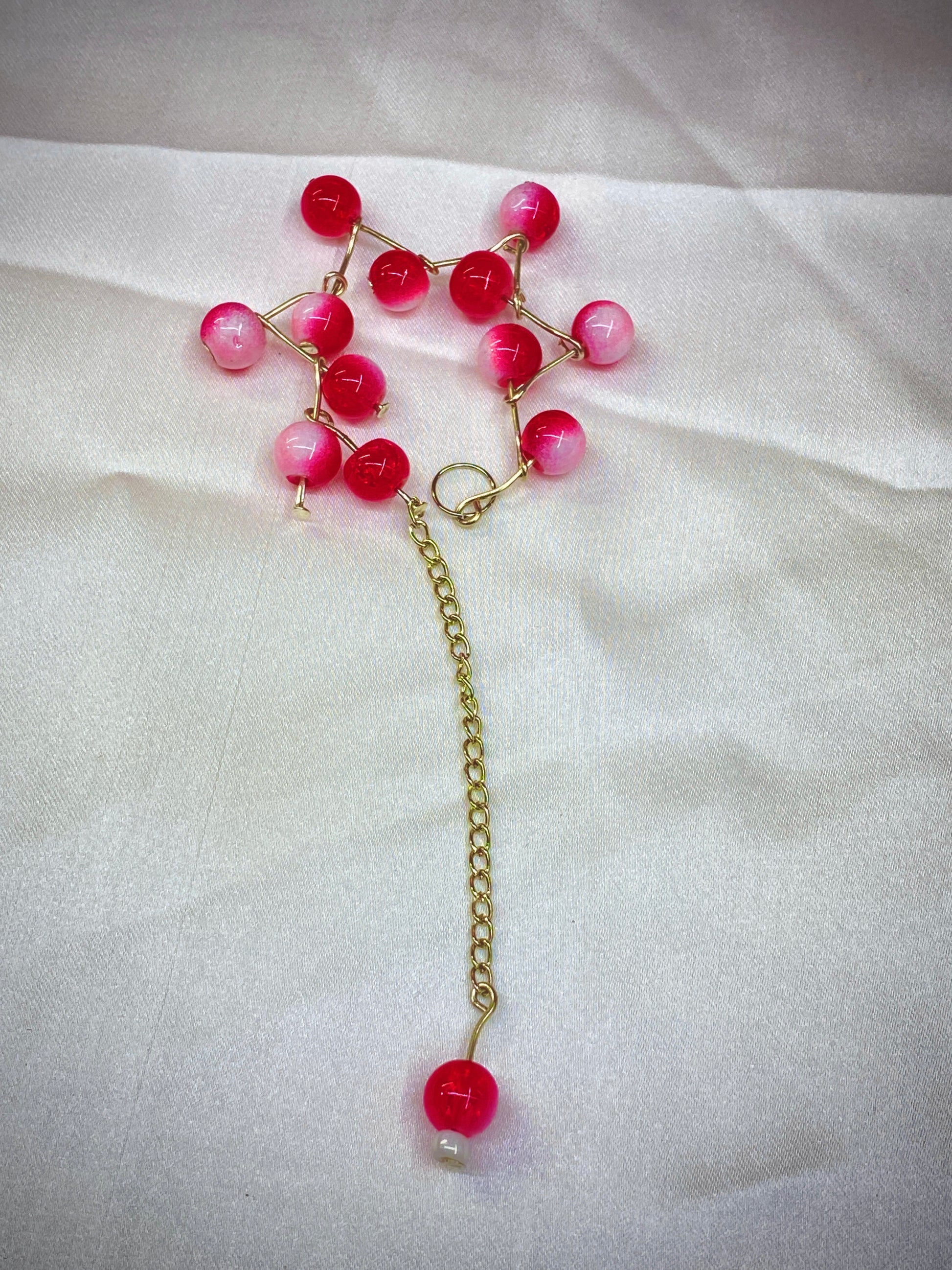 Necklace with pink beads and a gold chain on a white fabric background
