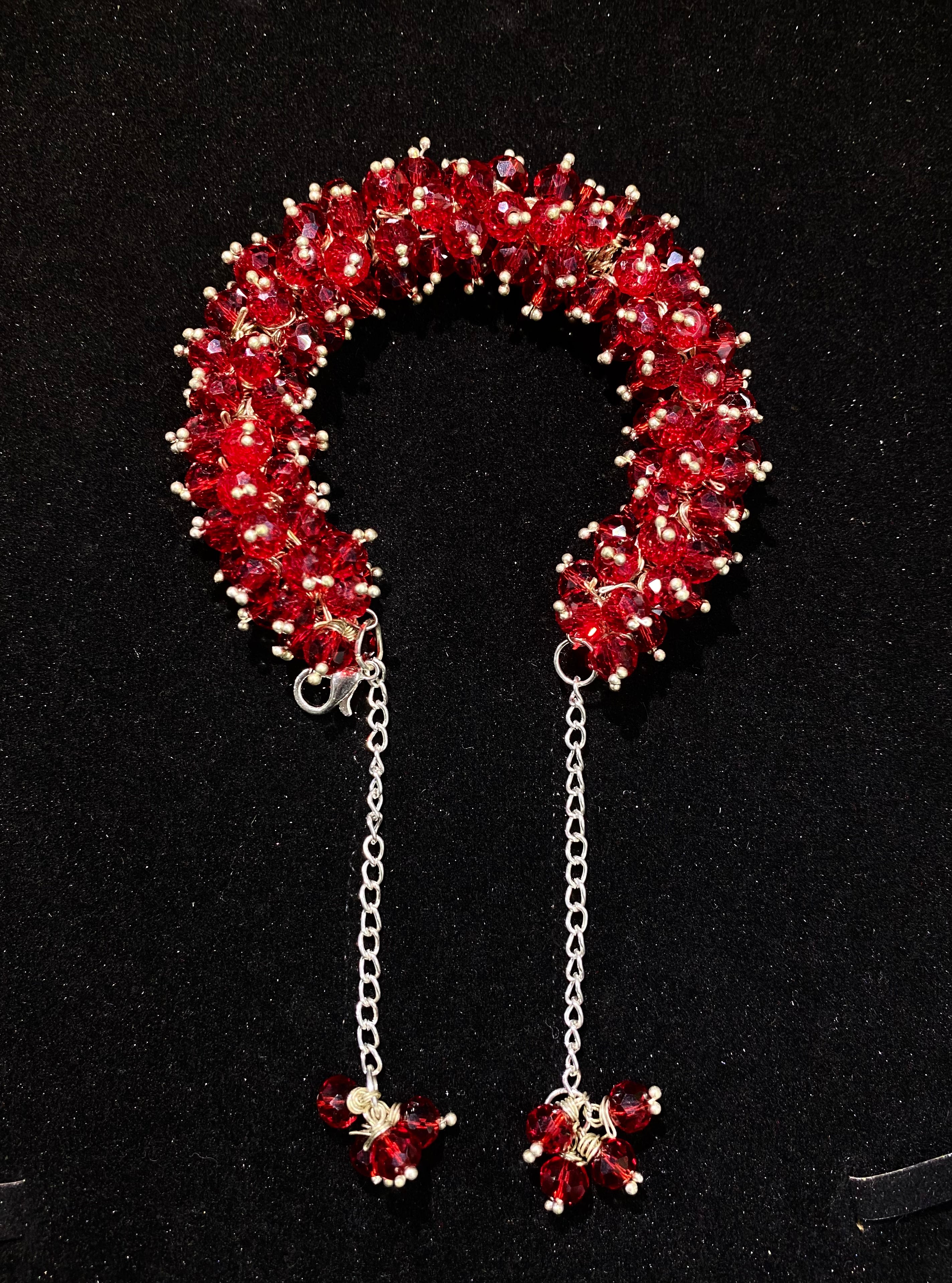 Red beaded candy cane-shaped brooch with chain and small beads on a black background