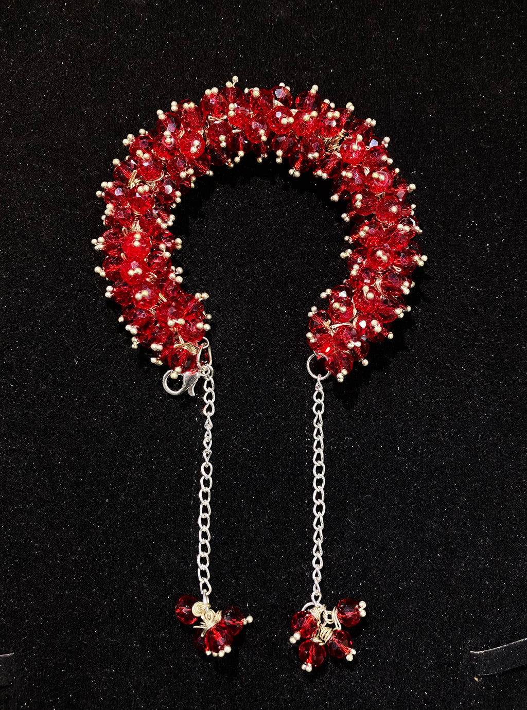 Red beaded candy cane-shaped brooch with chain and small beads on a black background